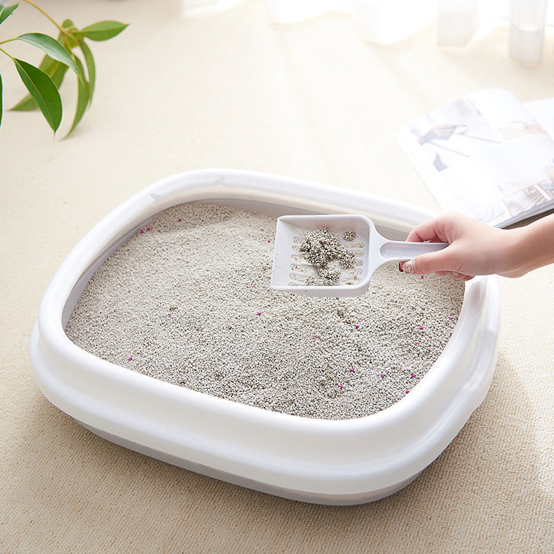 White cat litter box with scoop on a light surface