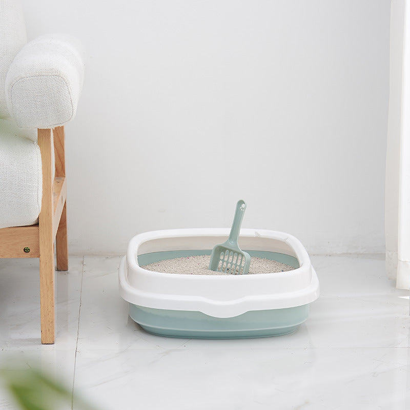 Pet litter box with a scoop on a light-colored floor next to a wooden bench.