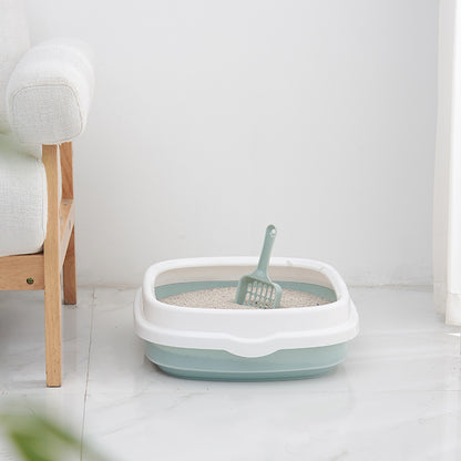 Pet litter box with a scoop on a light-colored floor next to a wooden bench.